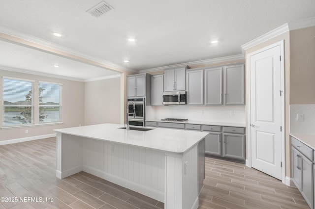 kitchen featuring an island with sink, stainless steel appliances, and gray cabinetry