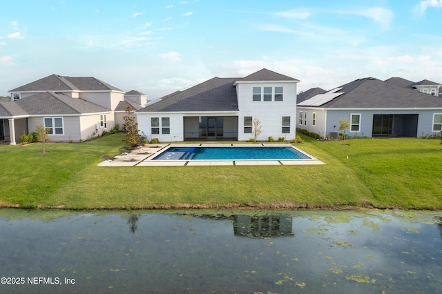 back of property with an outdoor pool, a water view, and a lawn