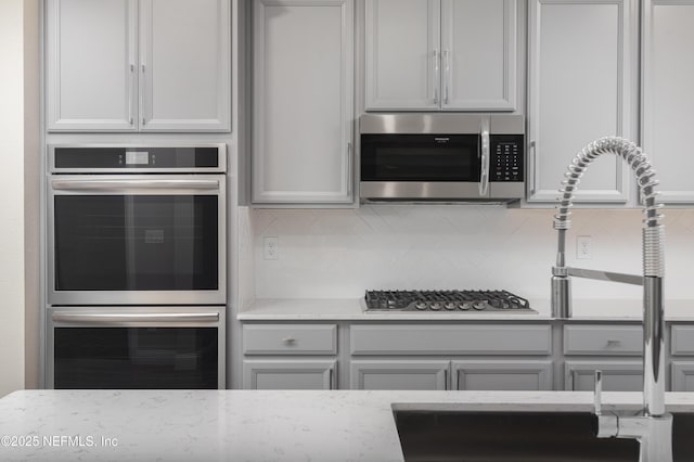 kitchen featuring stainless steel appliances, light stone counters, and decorative backsplash