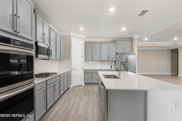 kitchen with appliances with stainless steel finishes, gray cabinets, a sink, and an island with sink