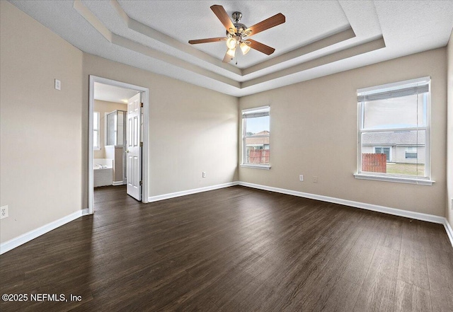 spare room with dark wood-style floors, a raised ceiling, ceiling fan, and baseboards