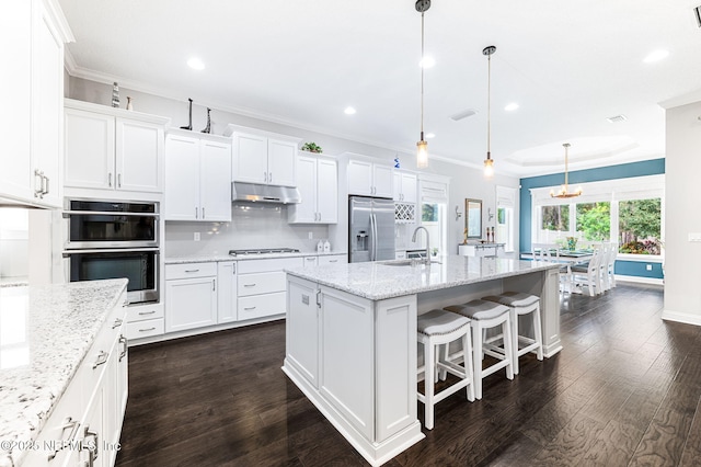 kitchen featuring stainless steel appliances, a kitchen island with sink, under cabinet range hood, and white cabinetry