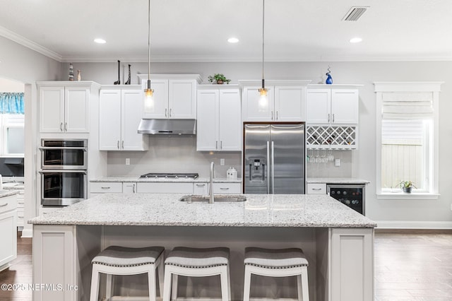 kitchen featuring a center island with sink, hanging light fixtures, appliances with stainless steel finishes, white cabinetry, and a sink