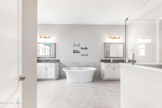 bathroom with a freestanding bath, two vanities, a sink, and tile walls