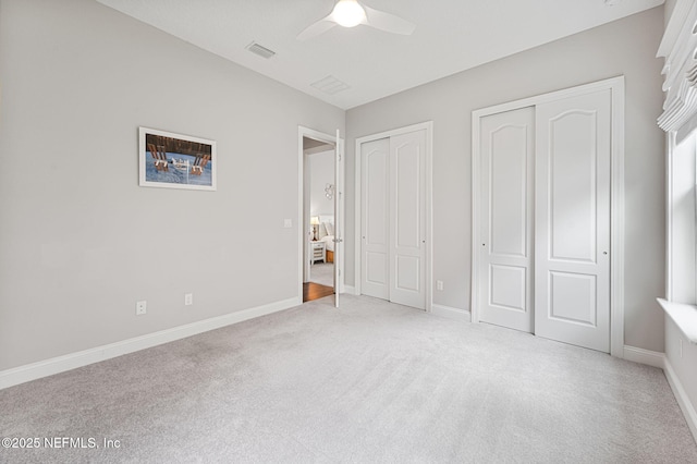 unfurnished bedroom featuring light carpet, baseboards, visible vents, and two closets