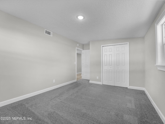 unfurnished bedroom featuring a textured ceiling, carpet flooring, visible vents, and baseboards