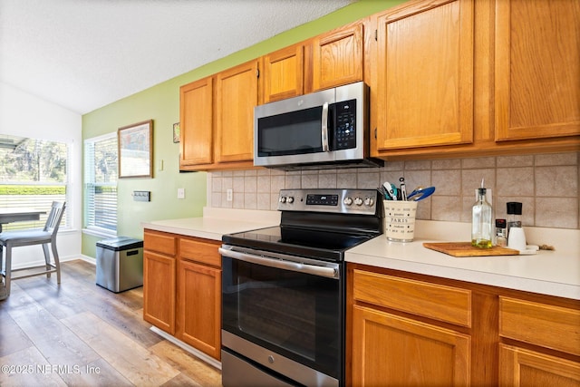 kitchen with lofted ceiling, light wood-style floors, light countertops, appliances with stainless steel finishes, and decorative backsplash