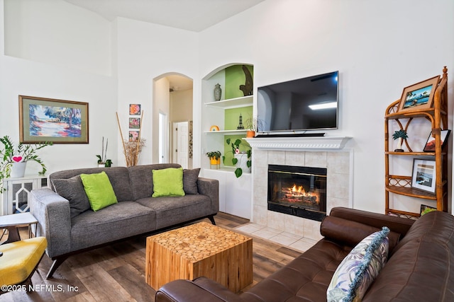 living area with built in features, arched walkways, a tiled fireplace, and wood finished floors