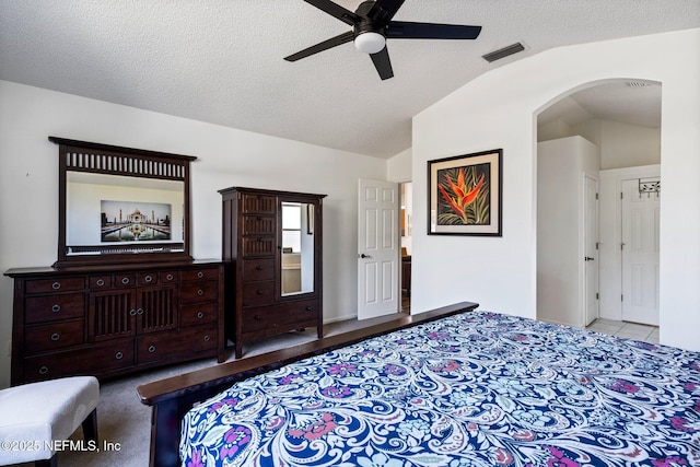 carpeted bedroom featuring visible vents, arched walkways, ceiling fan, vaulted ceiling, and a textured ceiling