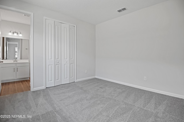 unfurnished bedroom featuring baseboards, visible vents, light colored carpet, a textured ceiling, and a closet