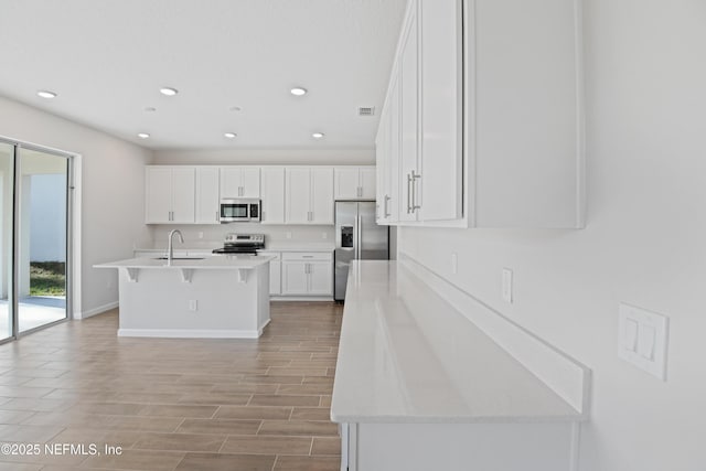 kitchen with a center island with sink, white cabinets, appliances with stainless steel finishes, light countertops, and a sink