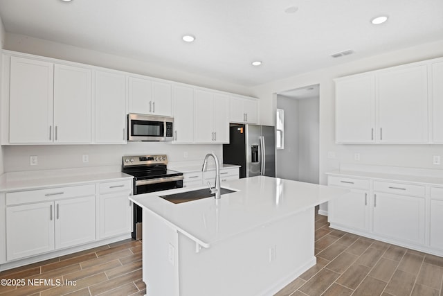 kitchen with a sink, stainless steel appliances, an island with sink, and light countertops