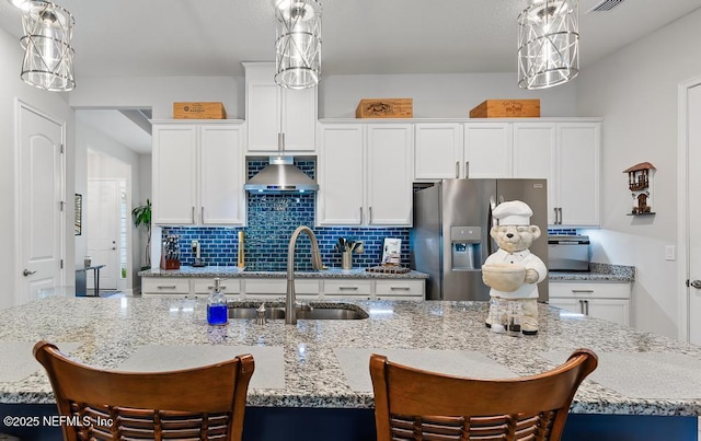 34072 Lavender Parke Dr, Fernandina Beach, FL 32034 - kitchen featuring wall chimney range hood, an island with sink, stainless steel fridge, and decorative light fixtures