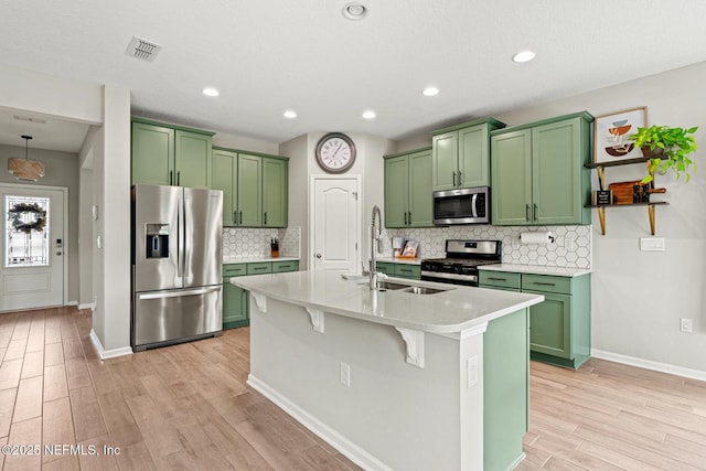 kitchen featuring a sink, light wood-style floors, green cabinets, light countertops, and appliances with stainless steel finishes