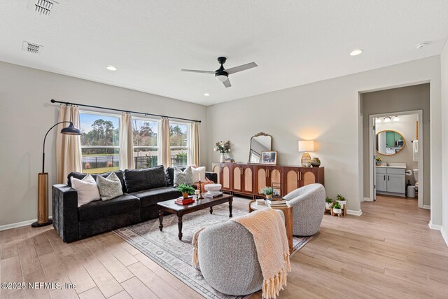 living area with light wood finished floors, a ceiling fan, visible vents, and baseboards