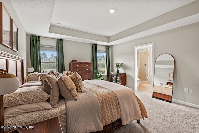 carpeted bedroom with a tray ceiling, ensuite bath, baseboards, and a textured ceiling