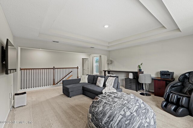 living area with a raised ceiling, carpet flooring, visible vents, and a textured ceiling