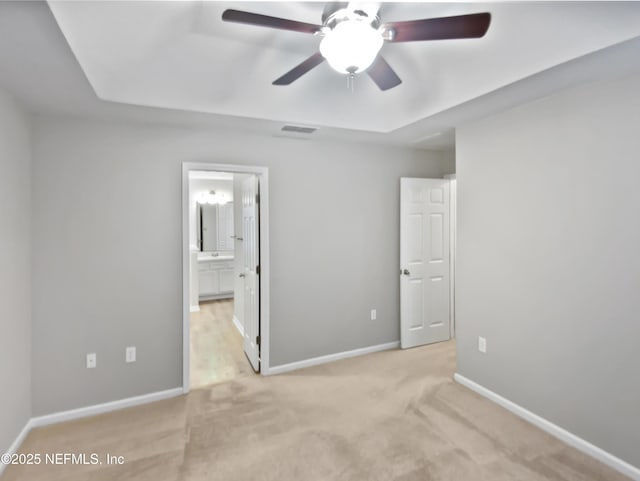 unfurnished bedroom featuring light carpet, baseboards, visible vents, a raised ceiling, and ensuite bathroom