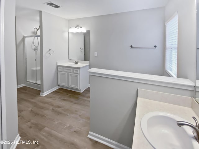 bathroom featuring visible vents, wood finished floors, a sink, a shower stall, and two vanities