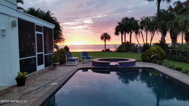 pool at dusk with a pool with connected hot tub, a sunroom, a water view, and fence