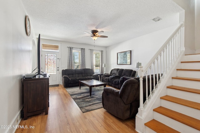 living area with visible vents, stairway, light wood-style floors, ceiling fan, and a textured ceiling