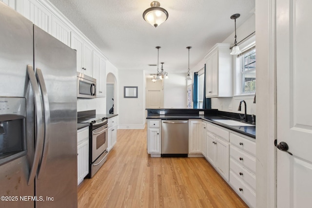 kitchen featuring dark countertops, a peninsula, stainless steel appliances, white cabinetry, and a sink