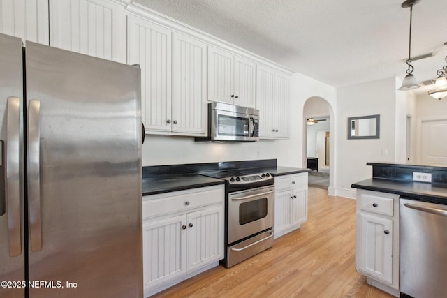 kitchen featuring arched walkways, light wood finished floors, dark countertops, appliances with stainless steel finishes, and white cabinetry