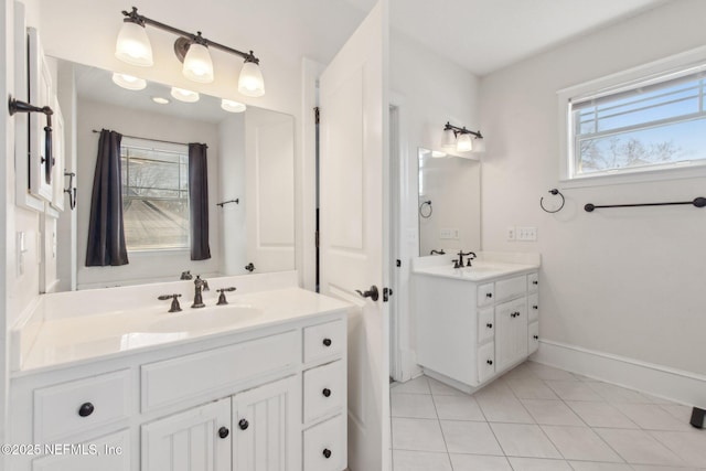 bathroom with tile patterned flooring, two vanities, a sink, and baseboards