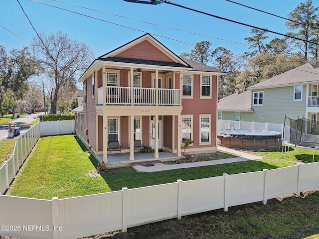 view of front facade with a fenced backyard, a balcony, a front lawn, a trampoline, and a patio area