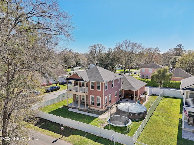 back of property with a fenced backyard, a balcony, a shingled roof, a yard, and a trampoline