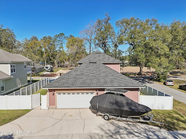 view of side of home featuring concrete driveway, a shingled roof, and fence