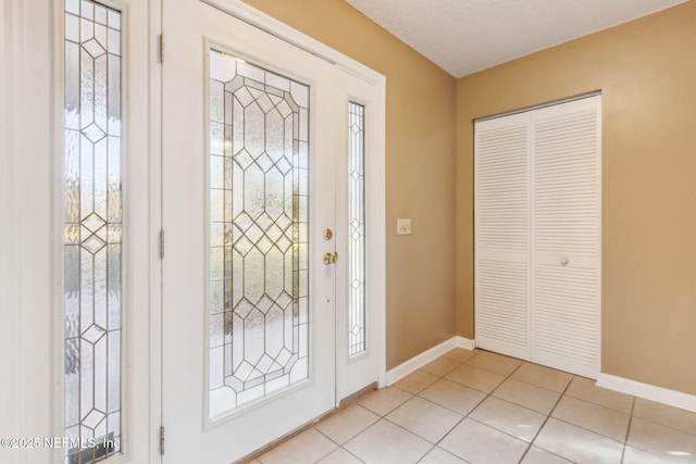 foyer entrance with a textured ceiling, baseboards, and light tile patterned floors