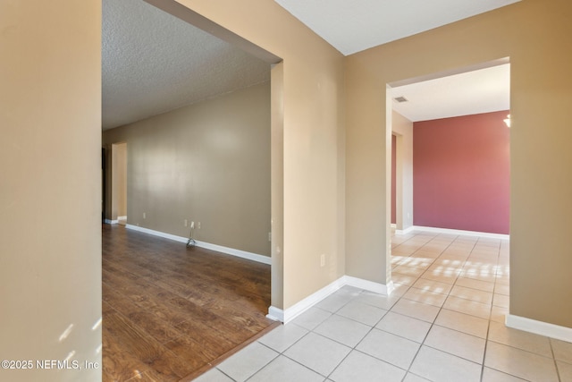 unfurnished room with light wood-type flooring, visible vents, a textured ceiling, and baseboards