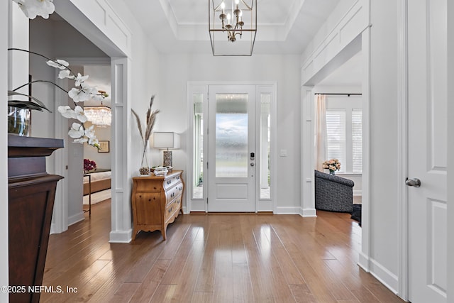 entryway featuring a notable chandelier, a raised ceiling, hardwood / wood-style floors, ornamental molding, and baseboards