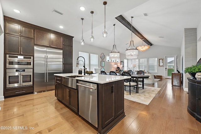 kitchen with appliances with stainless steel finishes, dark brown cabinetry, light wood-style flooring, and a sink