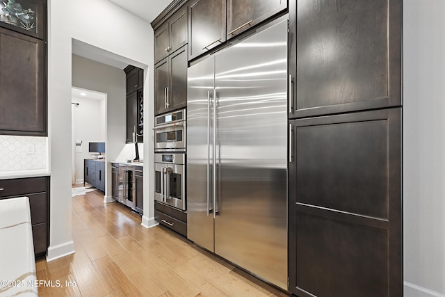 kitchen with dark brown cabinetry, light countertops, appliances with stainless steel finishes, decorative backsplash, and light wood finished floors