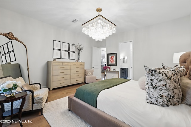 bedroom with connected bathroom, wood finished floors, visible vents, and a notable chandelier