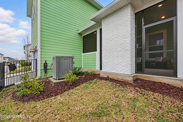 view of side of property with fence, central AC, and brick siding