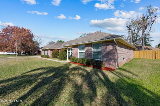 view of front facade with roof with shingles, a front yard, fence, and brick siding