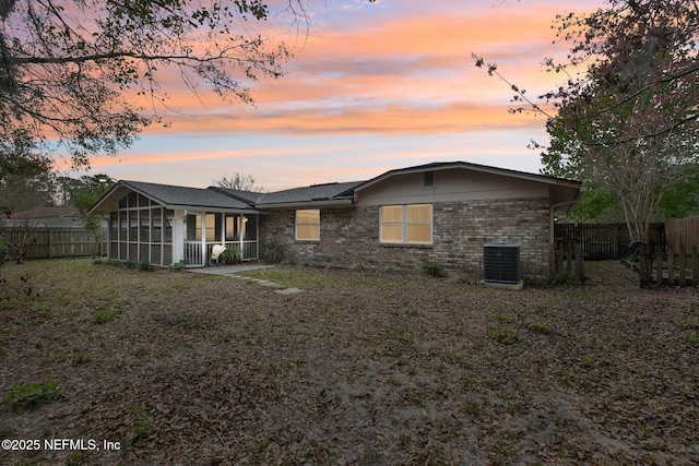 back of house at dusk featuring brick siding, a sunroom, central AC, and fence