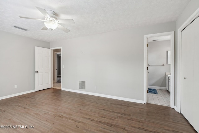 unfurnished bedroom featuring visible vents, baseboards, a textured ceiling, and wood finished floors