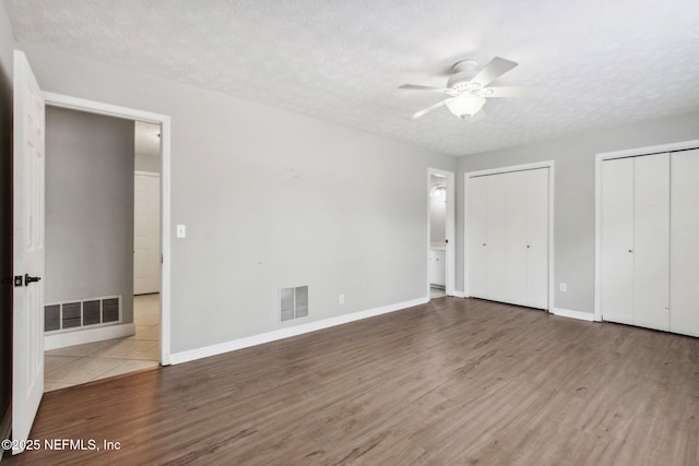 unfurnished bedroom featuring visible vents, multiple closets, a textured ceiling, and wood finished floors