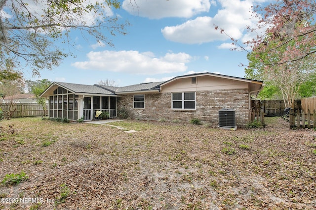 rear view of house featuring brick siding, central air condition unit, a fenced backyard, and a sunroom