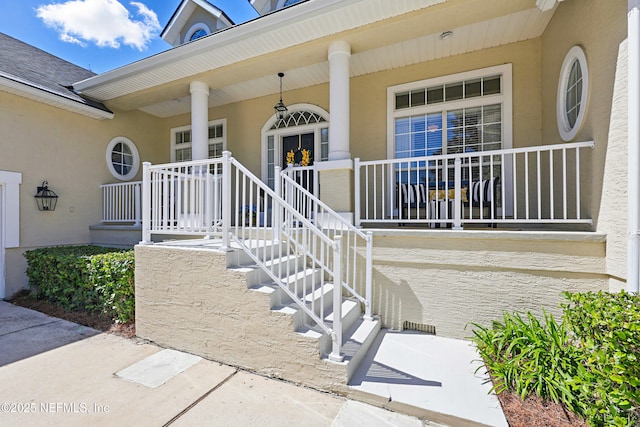 property entrance featuring covered porch, roof with shingles, and stucco siding