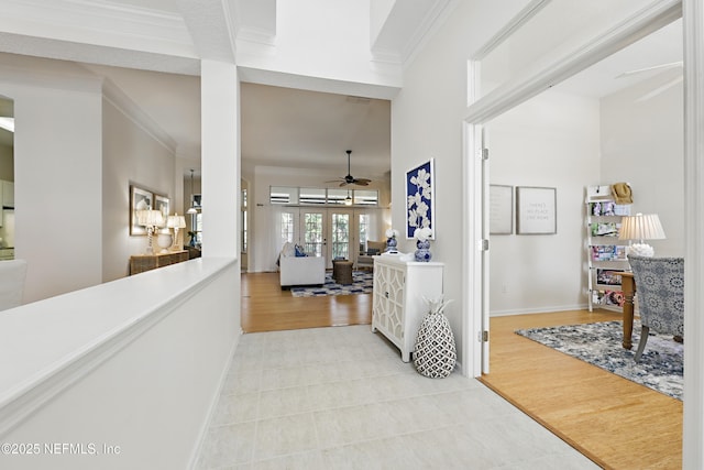 hallway featuring baseboards, ornamental molding, french doors, a towering ceiling, and light wood-style floors