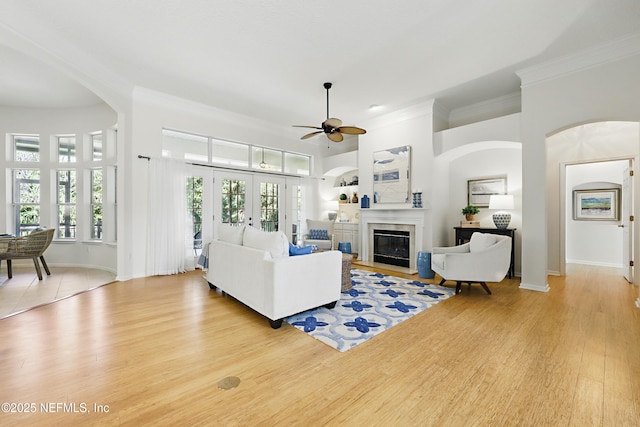 living room with a ceiling fan, a glass covered fireplace, wood finished floors, arched walkways, and crown molding