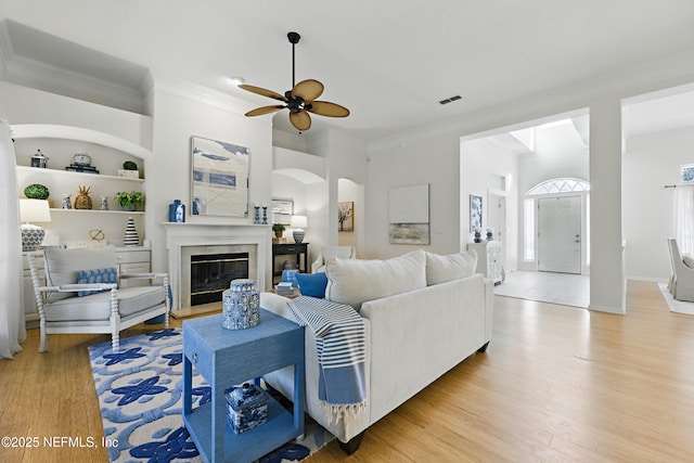 living room with built in features, wood finished floors, visible vents, ceiling fan, and ornamental molding