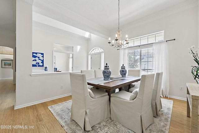 dining room with crown molding, baseboards, light wood-type flooring, arched walkways, and a notable chandelier