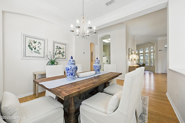 dining area with light wood-type flooring, visible vents, ornamental molding, arched walkways, and an inviting chandelier