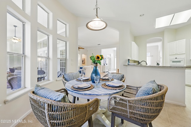 dining space with light tile patterned flooring, baseboards, arched walkways, and ceiling fan